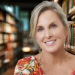 Woman with short blonde hair smiling in a library surrounded by bookshelves
