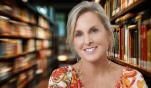 Woman with short blonde hair smiling in a library surrounded by bookshelves